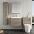Bathroom setup with wooden vanity, mirror, and toilet against a tiled wall.