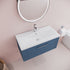 Bathroom vanity with blue cabinet, white countertop, and round mirror on a light pink wall.
