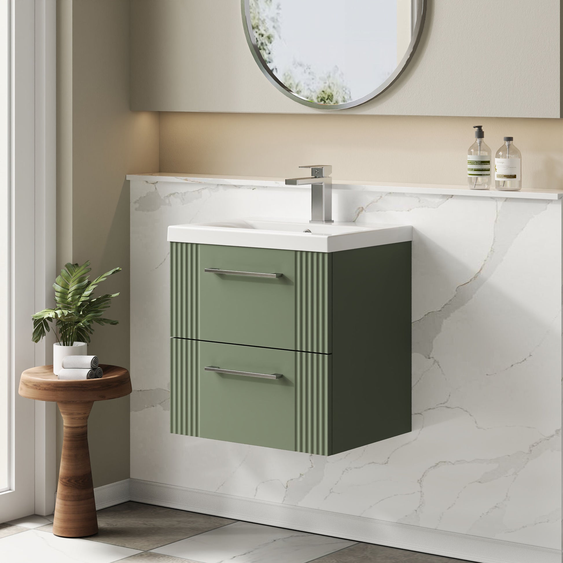Bathroom vanity with green cabinet and white countertop, featuring a round mirror and small plant.