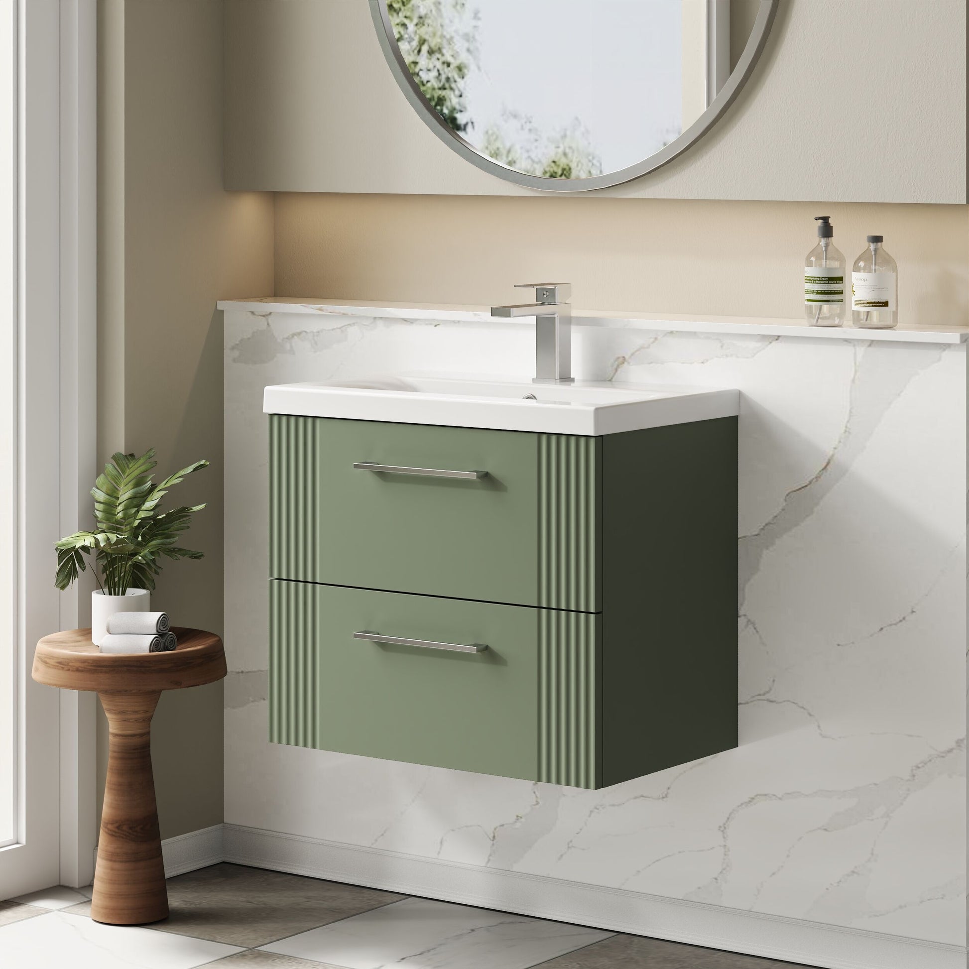 Bathroom vanity with green cabinet and white countertop, featuring a round mirror and small plant.