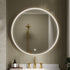 Bathroom with a round illuminated mirror, brushed brass frame , old fixtures, and a tiled wall.