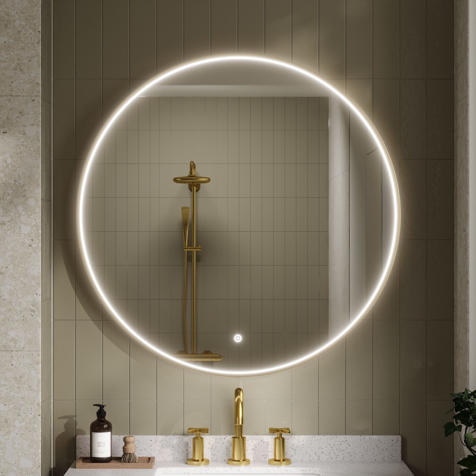 Bathroom with a round illuminated mirror, brushed brass frame , old fixtures, and a tiled wall.