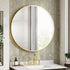 Round gold-framed mirror above a sink with gold fixtures in a bathroom setting.