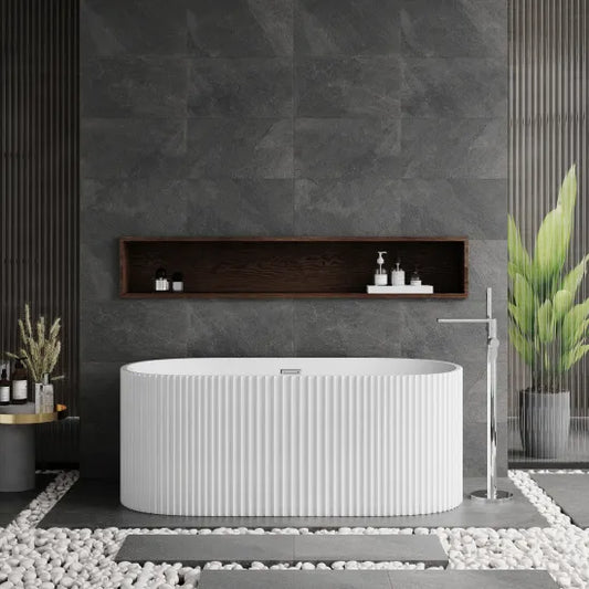 An oval-shaped, white freestanding bathtub with a textured exterior, positioned against a dark tiled wall with a wooden shelf above it. The bathtub is designed for adults and features a central drain.