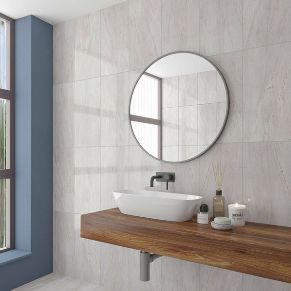 Bathroom with a round mirror, white sink, and wooden vanity. On grey marble gloss tiled wall.