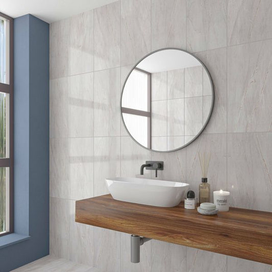 Bathroom with a round mirror, white sink, and wooden vanity. On grey marble gloss tiled wall.