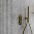 Gold shower control panel and handheld shower head on a fluted tiled wall.