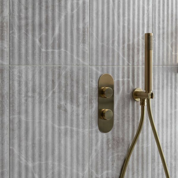 Gold shower control panel and handheld shower head on a fluted tiled wall.