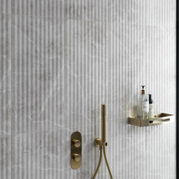 Gold shower fixture and control panel on a marble fluted tiled bathroom wall.