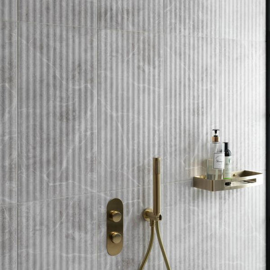 Gold shower fixture and control panel on a marble fluted tiled bathroom wall.