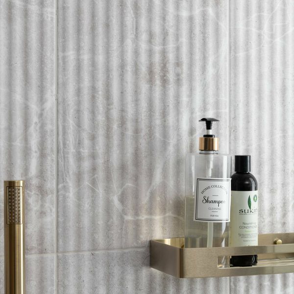 Two bottles on a gold shelf against a fluted grey tiled wall.