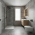 Modern bathroom interior with gray stone-look tiles, a walk-in shower with black fixtures, a white wall-mounted toilet, a light wood vanity with a white sink, and an illuminated rectangular mirror.