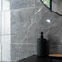 Black soap dispenser on a black surface with a marble-patterned wall tiles in the background