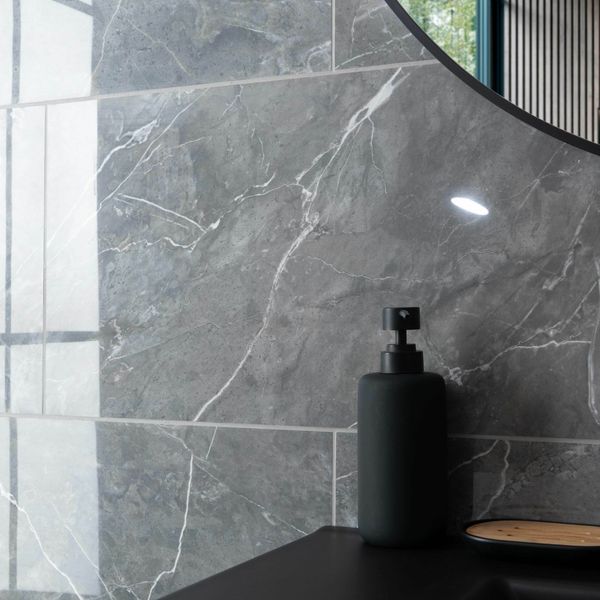 Black soap dispenser on a black surface with a marble-patterned wall tiles in the background