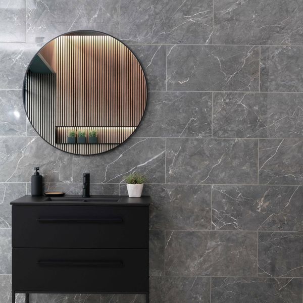 Bathroom with black vanity, round mirror, and grey marble wall.
