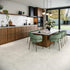 Modern kitchen with wooden cabinets, white tiled walls, grey stone tiled floor and a dining area with green chairs.