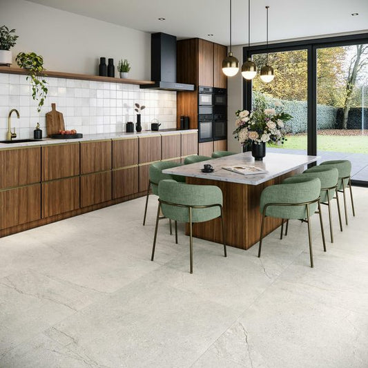 Modern kitchen with wooden cabinets, white tiled walls, grey stone tiled floor and a dining area with green chairs.
