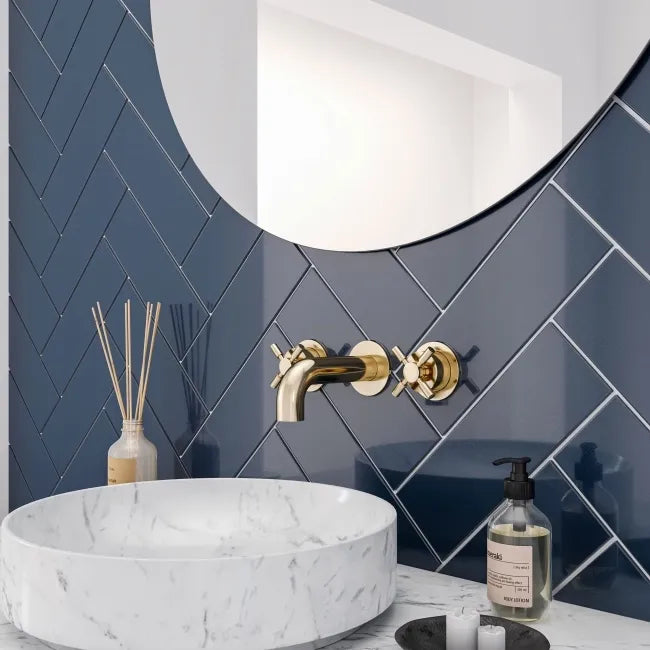 Bathroom with marble sink, navy blue metro tiles in a herringbone pattern, gold faucet, and blue tiled wall.
