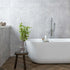 Modern bathroom with a freestanding bathtub, plant, and stool. Fluted grey marble wall tiles