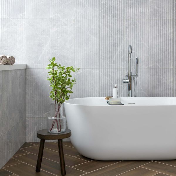 Modern bathroom with a freestanding bathtub, plant, and stool. Fluted grey marble wall tiles