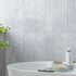 Bathroom with a white bathtub, plant, and toiletries against a fluted marble tiled wall.