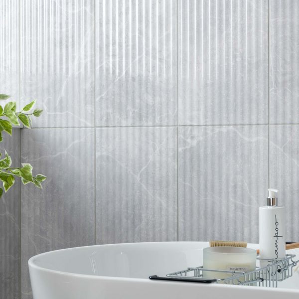 Bathroom with a white bathtub, plant, and toiletries against a fluted marble tiled wall.
