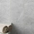 Grey fluted wall tiles with a textured pattern and rolled towels on a ledge.