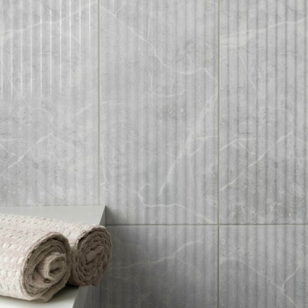 Grey fluted wall tiles with a textured pattern and rolled towels on a ledge.