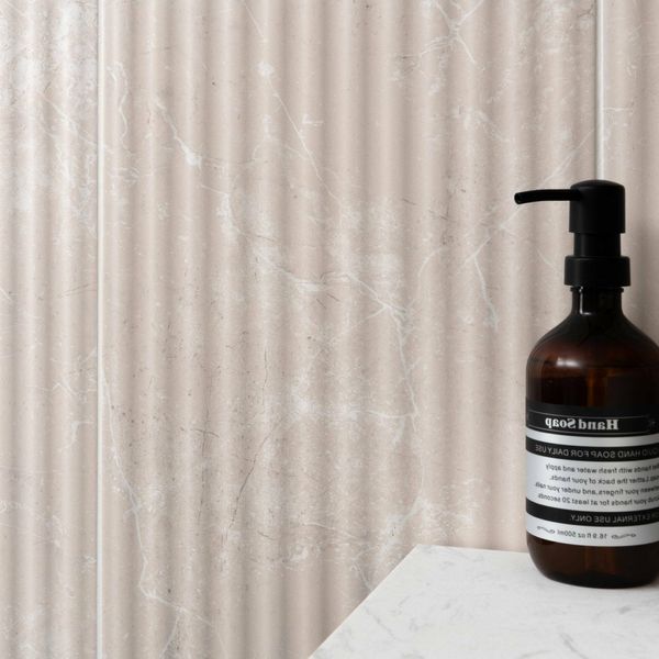 Brown bottle with pump on a white surface against a textured marble fluted beige tiled wall