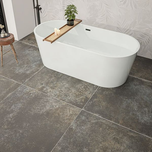 White freestanding bathtub in a modern bathroom with dark grey tiles and a small plant on a wooden tray.