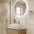 Modern bathroom with round illuminated mirror, sink, and wooden cabinet.