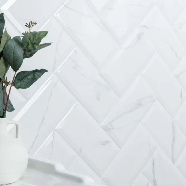 White marble tiles with a marble subway geometric pattern and a white vase with green leaves.