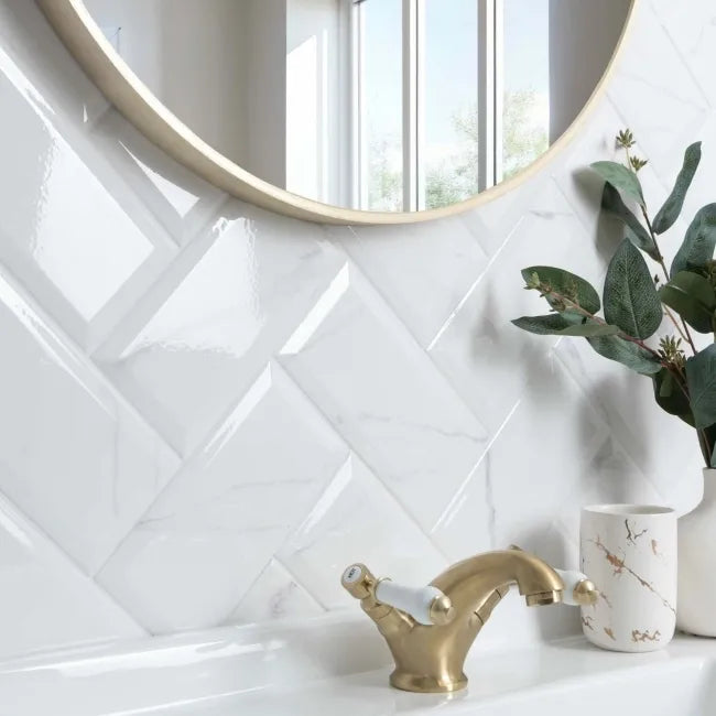 Bathroom with white tiled wall, gold faucet, and round mirror.